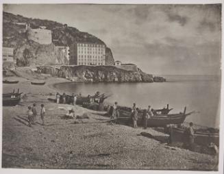 The beach at Nice with the Tour Bellanda and the Hotel Suisse in the background. Fishermen stand on the beach amongst their boats
