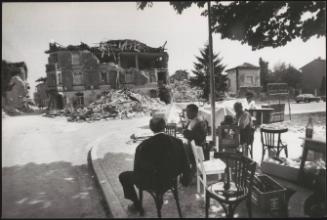 Three men sit on the corner of a street overlooking destruction caused by the Friuli earthquake in 1976