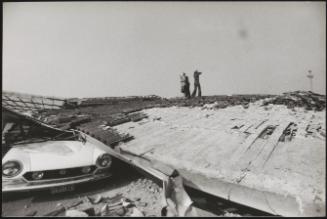 Three people stand on the flattened roof in the days after the mass destruction caused by the Friuli earthquake, 1976
