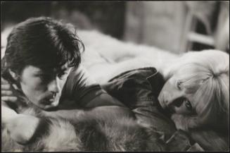 Alain Delon and Mireille Darc lie on a bed on a film set 