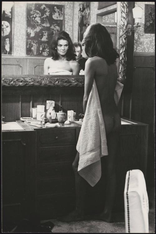 A nude Florinda Bolkan stands in front of a bathroom mirror