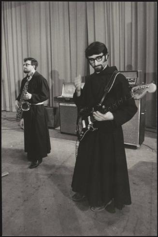 A pair of priests in their cassocks jamming on saxophone and electric guitar