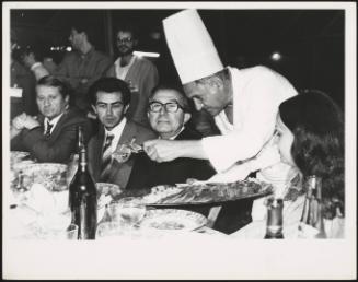 Giulio Andreotti is served ham by a chef at a dinner
