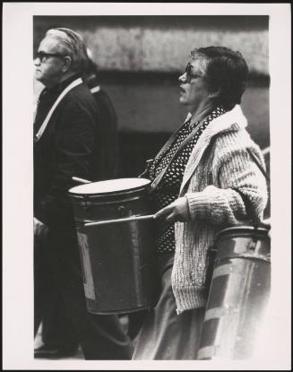 A woman bangs a metal drum at a rally for affordable housing