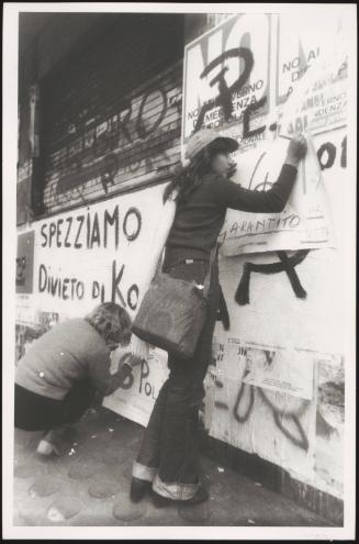 Two women pasting up communist posters on a wall