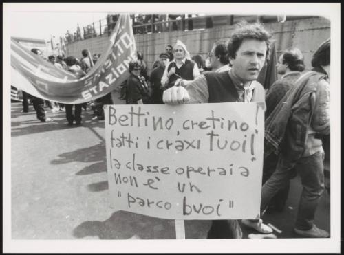 A workers' demonstration, where a man holds a placard aimed at politician Bettino Craxi