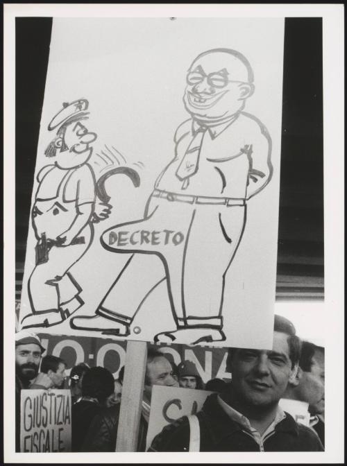 A hand drawn protest placard of a satirical illustration of Bettino Craxi also containing the word 'Decreto', meaning 'decree'