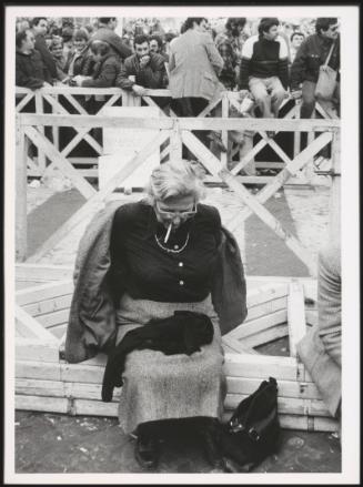 An elderly lady smoking a cigarette whilst taking off her jacket 