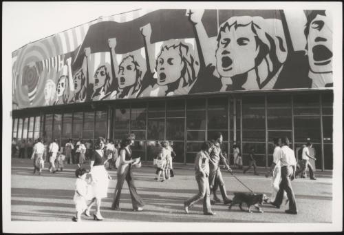 Pedestrians walking past a large commercial building with a revolutionary graphic-art banner across its top