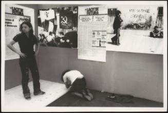 Two women in front of communist activists' posters and reports