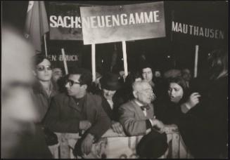 People attend a demonstration holding up placrds with the names of Nazi concentration camps: 'Mauthausen' and 'Neuengamme'