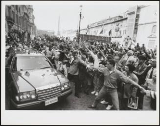 A large crowd gather on the streets to watch a car lead a Neo Fascist funeral procession 