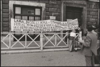 A large protest banner is held up in front of a building during a workers' demonstration for better pay, denouncing Luciano Lama