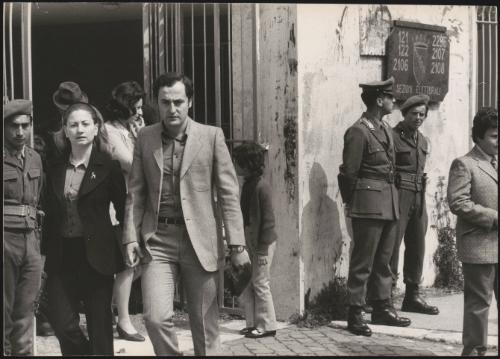 A couple walk hand in hand down a street past a polling station guarded by army and police