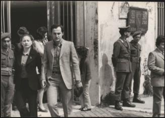 A couple walk hand in hand down a street past a polling station guarded by army and police