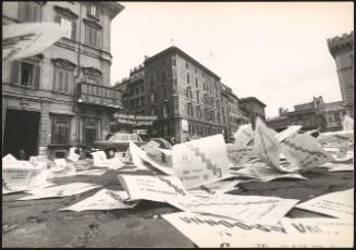 In an Italian piazza, flyers calling for Giulio Caradonna to be elected in an upcoming election litter the pavement