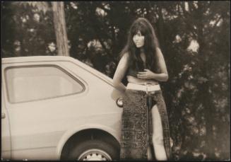 A young prostitute leans  against a car 