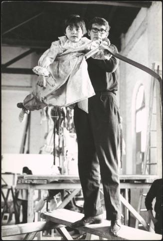 Children being prepared for a religious procession, dressed as angels and suspended on structures to appear as though they are flying
