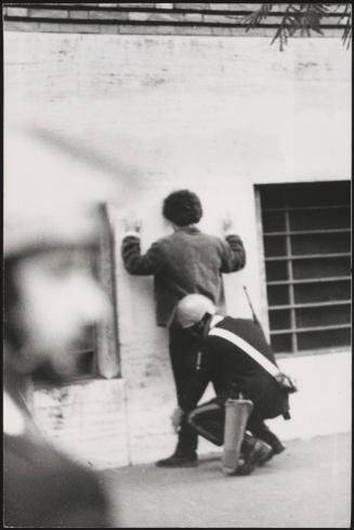 A man is subjected to a body search against a wall by a police man 