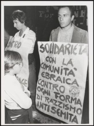 Two men stand with a hand written placards against the Great Synagogue of Rome attack