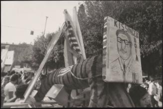 A hand drawn poster of Kissinger attached to a structure during a protest