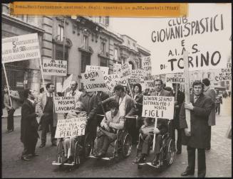 At a demonstration for the disabled in Rome, a group of people in the street, some in wheelchairs, are all holding protest placards