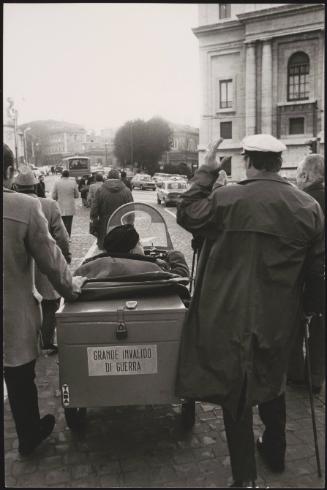 Men who were injured in the Great War march with walking sticks down the street with a motorized wheelchair as part of a protest for the disabled
