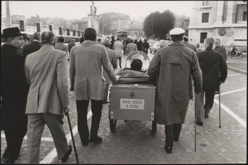 Men who were injured in the Great War march with walking sticks down the street with a motorized wheelchair as part of a protest for the disabled