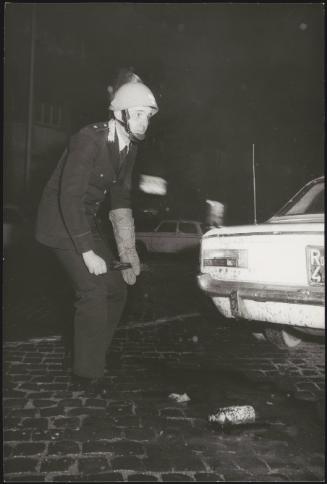 Riot policeman inspects an unexploded petrol bomb