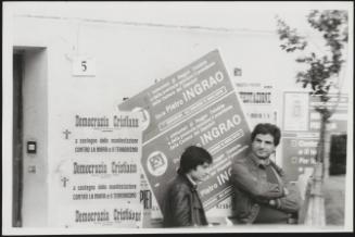 Two men lean against a wall bearing posters for the Communist and Democratic Parties during an anti Mafia demonstration in Calabria