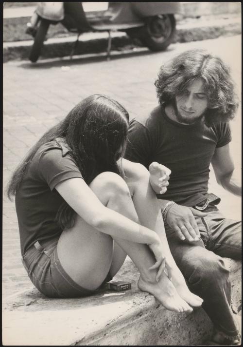 An Italian 'Pappagalli' man sits with a female tourist on a curb