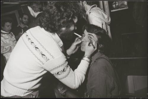 A man draws eyeliner on his friend 