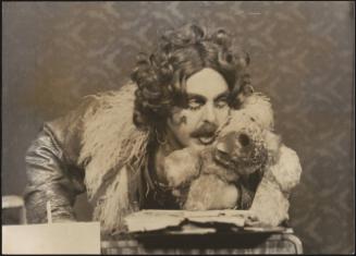 A man in theatrical makeup, clasping a teddy during a cabaret performance 