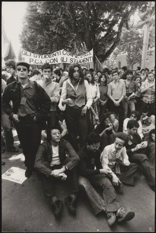 A crowd of student supporters of the Italian Communist Party (the PCI), sitting and standing in the road and carrying banners