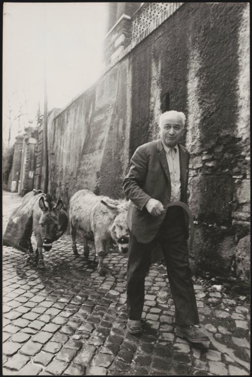 A man holding a scythe is followed by two donkeys