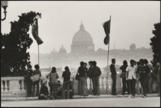 Young people hanging around in the aftermath of a demonstration, on a bridge in Rome, St. Peter's Basilica dome in the distance