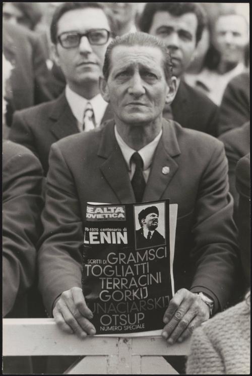 A man in a crowd holds a magazine dedicated to Soviet politics, dated 1970