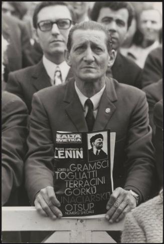 A man in a crowd holds a magazine dedicated to Soviet politics, dated 1970
