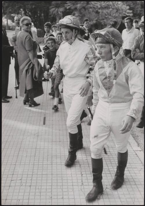 A female and male jockey walking through crowds towards their horses