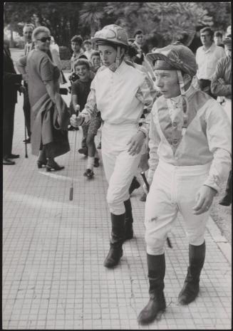 A female and male jockey walking through crowds towards their horses
