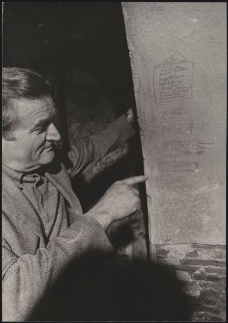 One of the survivors of the massacre at Marzabotto points out carved-out signatures left by prisoners on a wall