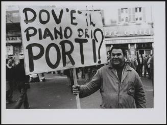 A disgruntled port worker holding a banner reading 'Where is the plan for the Ports?' at a protest of the port workers of Livorno