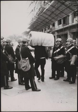 A squatter walks through a crowd of police, carrying his mattress over his head