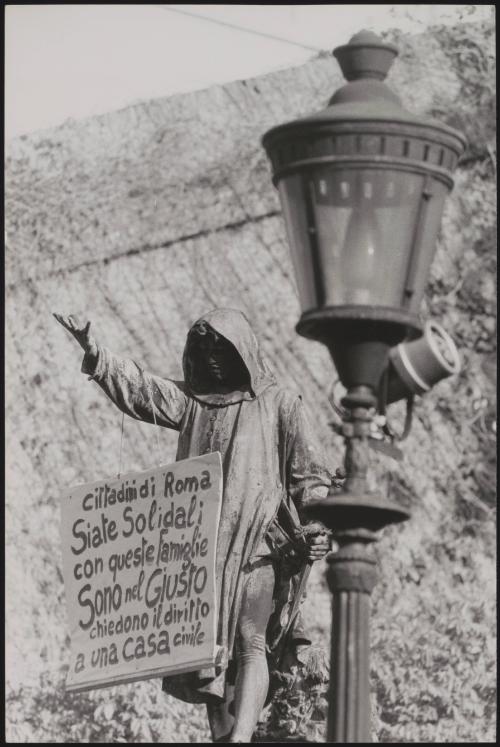 A protest placard for social housing hangs round the neck of a statue in Rome