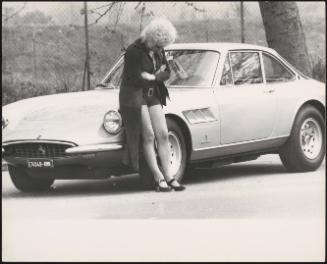 A prostitute looks at her feet and waits by a car