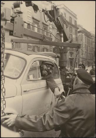 A man remains in his car as it's towed away.