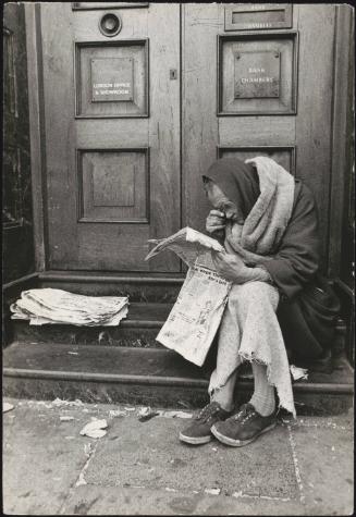 A homeless man reads a newspaper in a doorway 