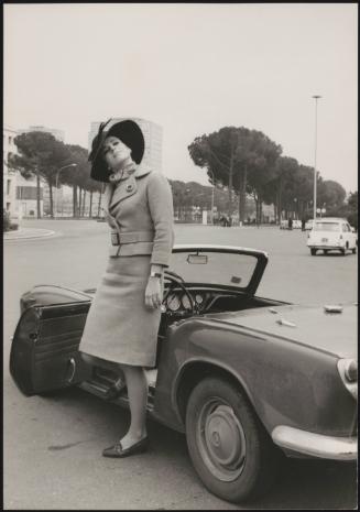 The Italian actress Marilù Tolo in a belted coat and hat stepping out of a Mini convertible