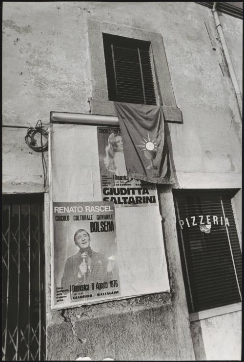 Wall of posters advertising Italian musicians  hangs from a window outside a Pizzeria