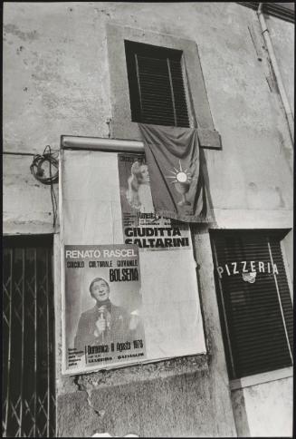 Wall of posters advertising Italian musicians  hangs from a window outside a Pizzeria